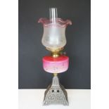 Late Victorian / early 20th Century oil lamp having a cast metal base with pink glass reservoir with