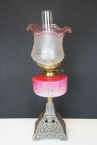 Late Victorian / early 20th Century oil lamp having a cast metal base with pink glass reservoir with