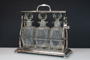 Early-to-mid 20th C silver plated tantalus, housing three cut glass decanters with stoppers,