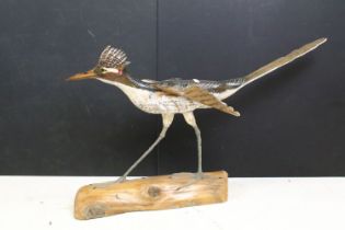 Carved wooden bird sculpture having hand painted details raised on a naturalistic wooden base.