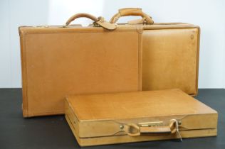 Three Hartmann brown leather suitcases, each with handles and metal locks and fittings. Largest