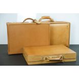 Three Hartmann brown leather suitcases, each with handles and metal locks and fittings. Largest