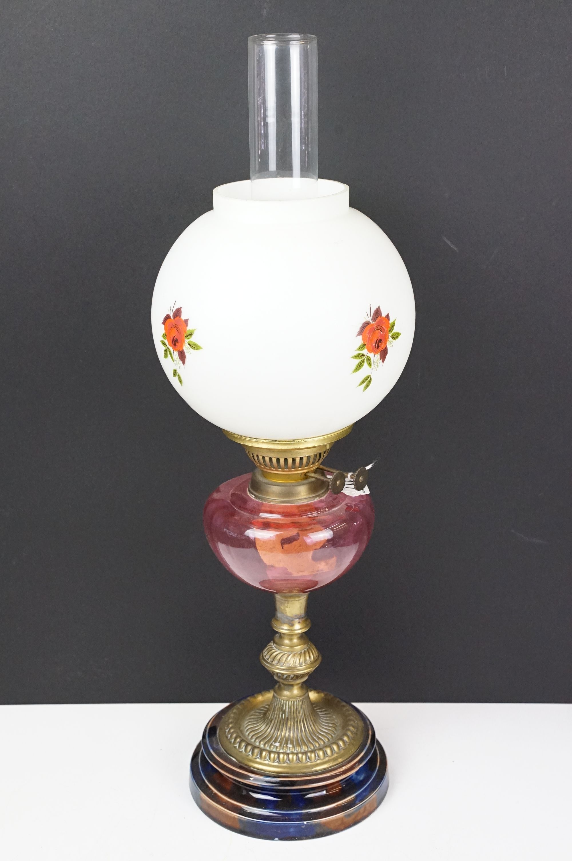 Early 20th century brass oil lamp, the white glass shade with floral detail, with cranberry glass