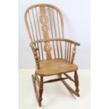 Light elm windsor rocking chair having a pierced splat and spindle back. Measures 100cm high.