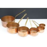 Collection of antique copper graduating sauce pans each having brass handles. Largest measures