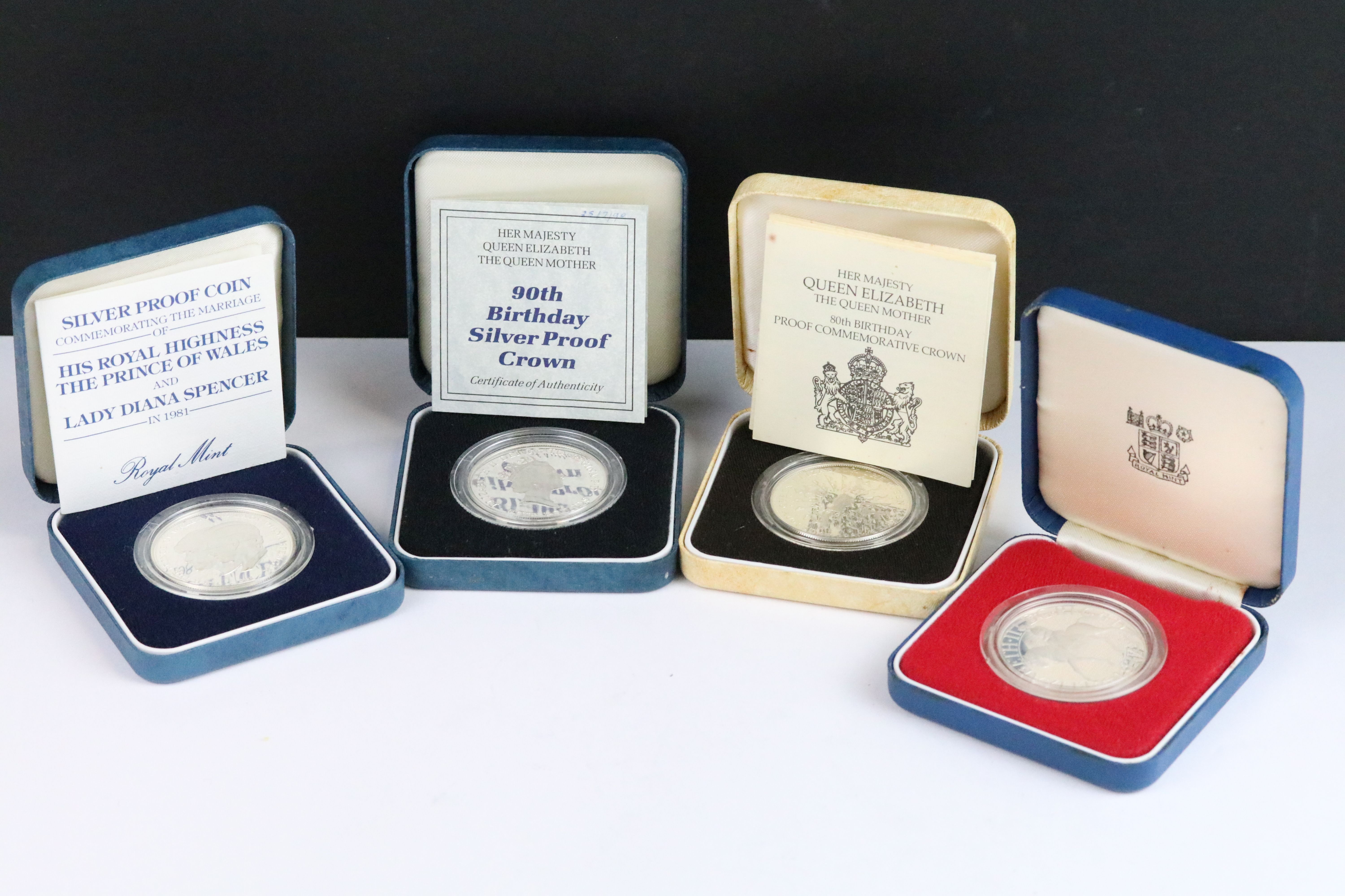 A collection of four Royal Mint silver proof crown coins all encapsulated within display cases.