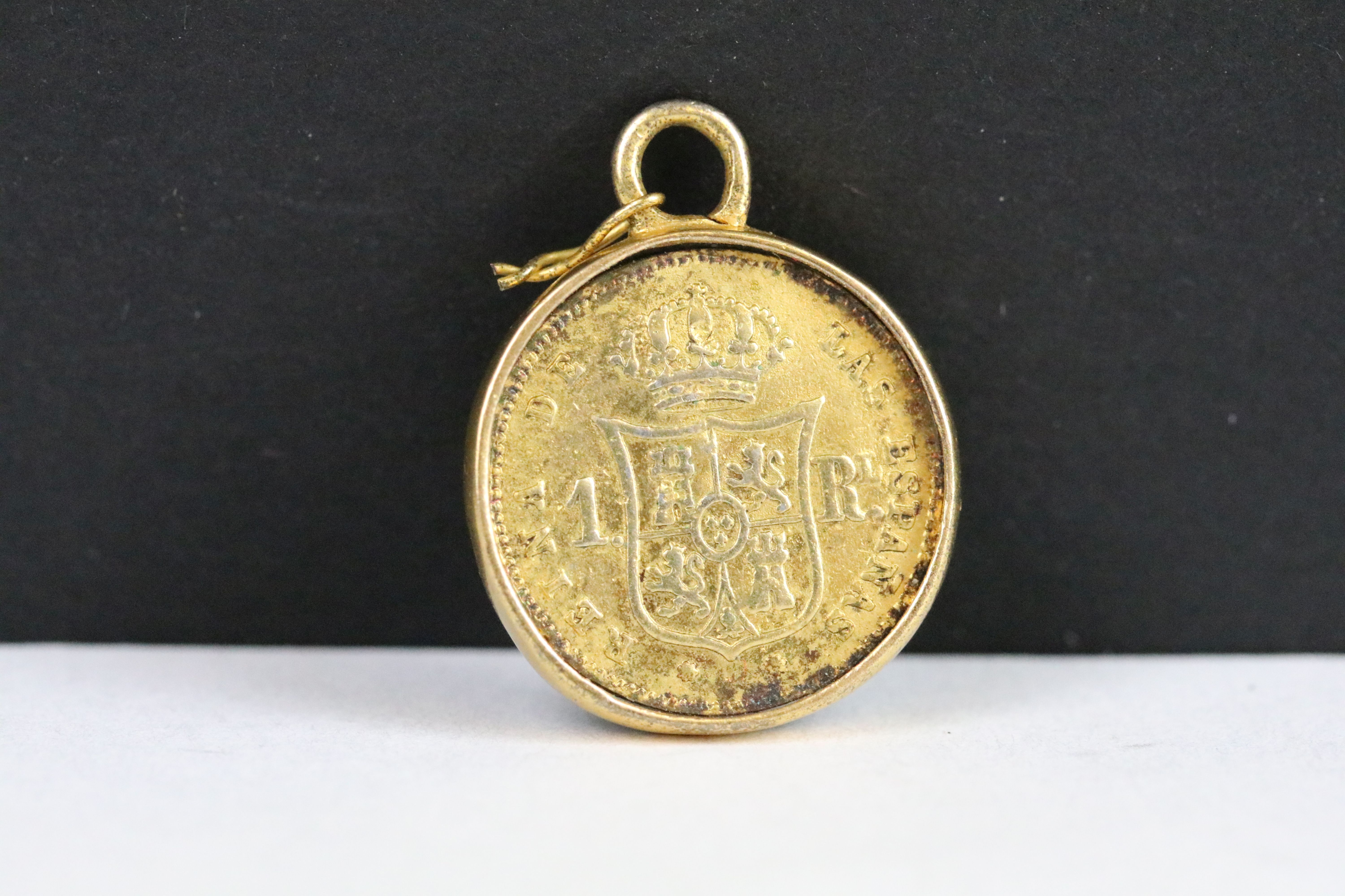 A Spanish 1864 gold 1 Real coin within a gold mount.