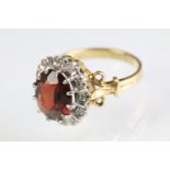 18ct gold garnet and diamond cluster ring. The ring being set with an oval mixed cut garnet with a