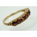 9ct gold and garnet seven stone ring set with seven round cut garnets to a plain shank. Hallmarked