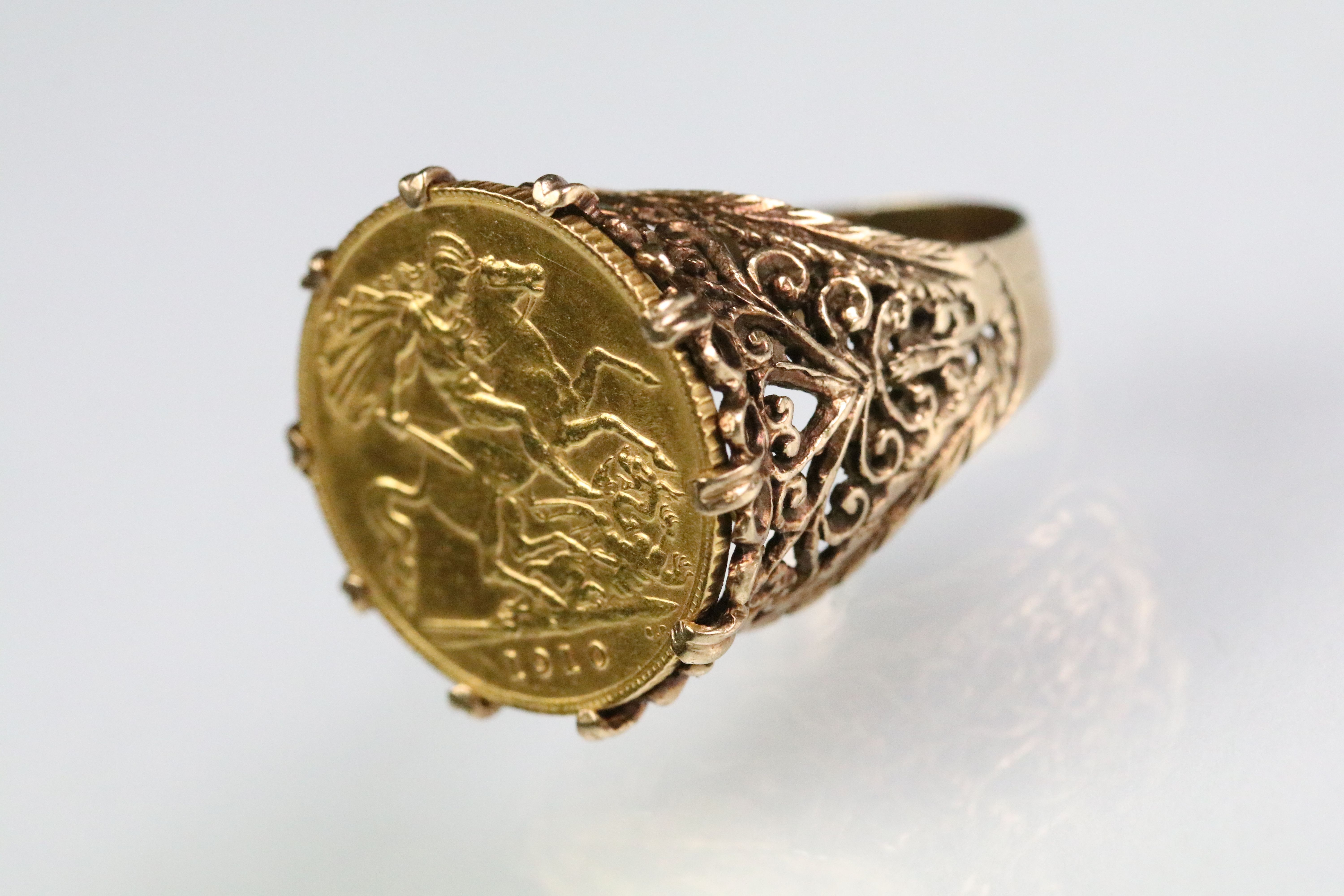 1910 half sovereign set into a 9ct gold pierced scrolled detail ring mount. Hallmarked 9ct to