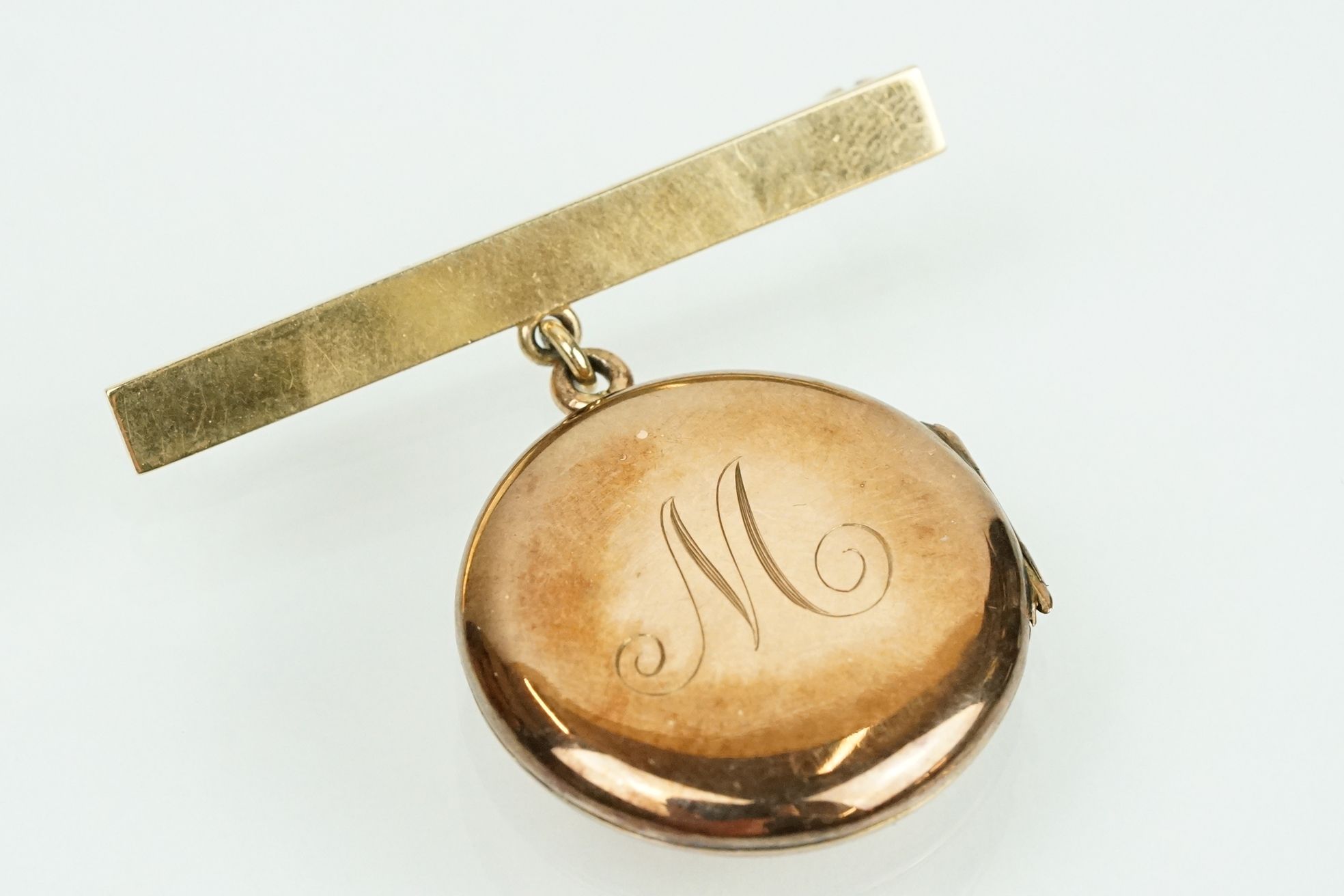 9ct gold hallmarked locket brooch. The bar brooch having a round locket suspended below with