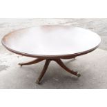Large circular mahogany dining table with veneer to edge, raised on a five-footed base with casters,