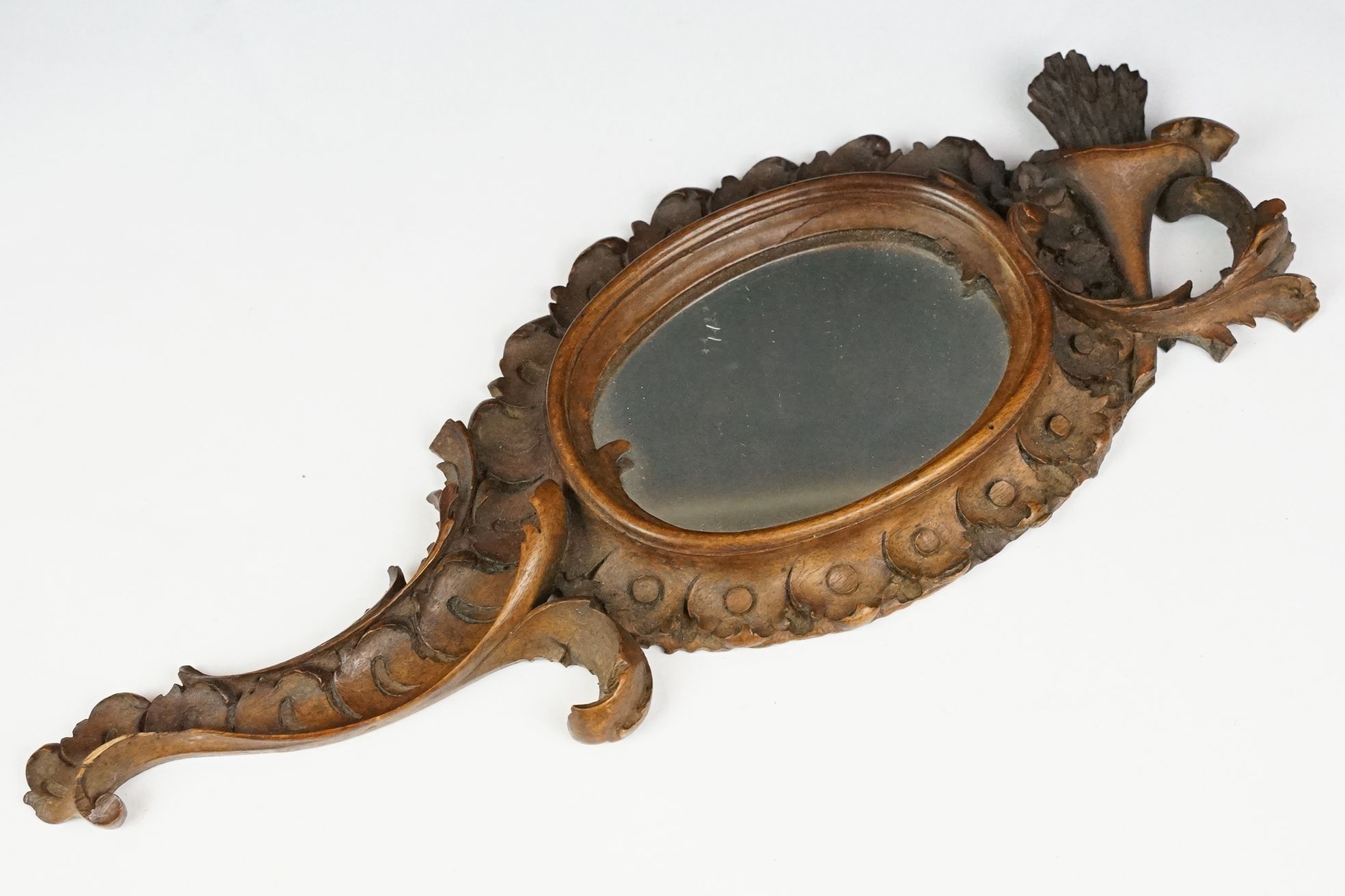 An antique carved wooden Black Forest hand mirror with foliate decoration.
