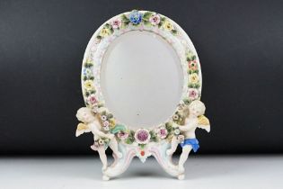 Continental porcelain floral encrusted wall mirror with bevelled glass and two putti to base, hand