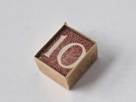 A ten shilling banknote charm, 9ct, (split to plastic cover)