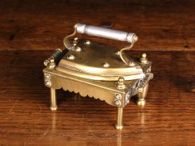 A Miniature Brass Flat Iron with steel handle on a rectangular trivet stand/footman.