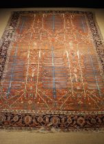 An Antique Heriz Carpet woven with blue fir trees on a red ground in a trellis border, worn.