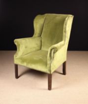 An Upholstered Wing Armchair covered in chartreuse green velvet edged with brass studs and standing