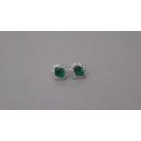 A certificated pair of 18ct white gold cluster earrings set with oval emeralds surrounded by round