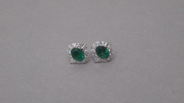 A certificated pair of 18ct white gold cluster earrings set with oval emeralds surrounded by round