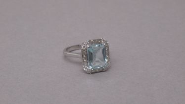 An 18ct white gold ring set with a central emerald-cut aquamarine, with surrounding princess-cut
