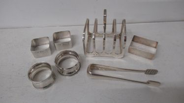 Seven silver items including toast rack, sugar tongs and five napkin rings - approx weight 7.8