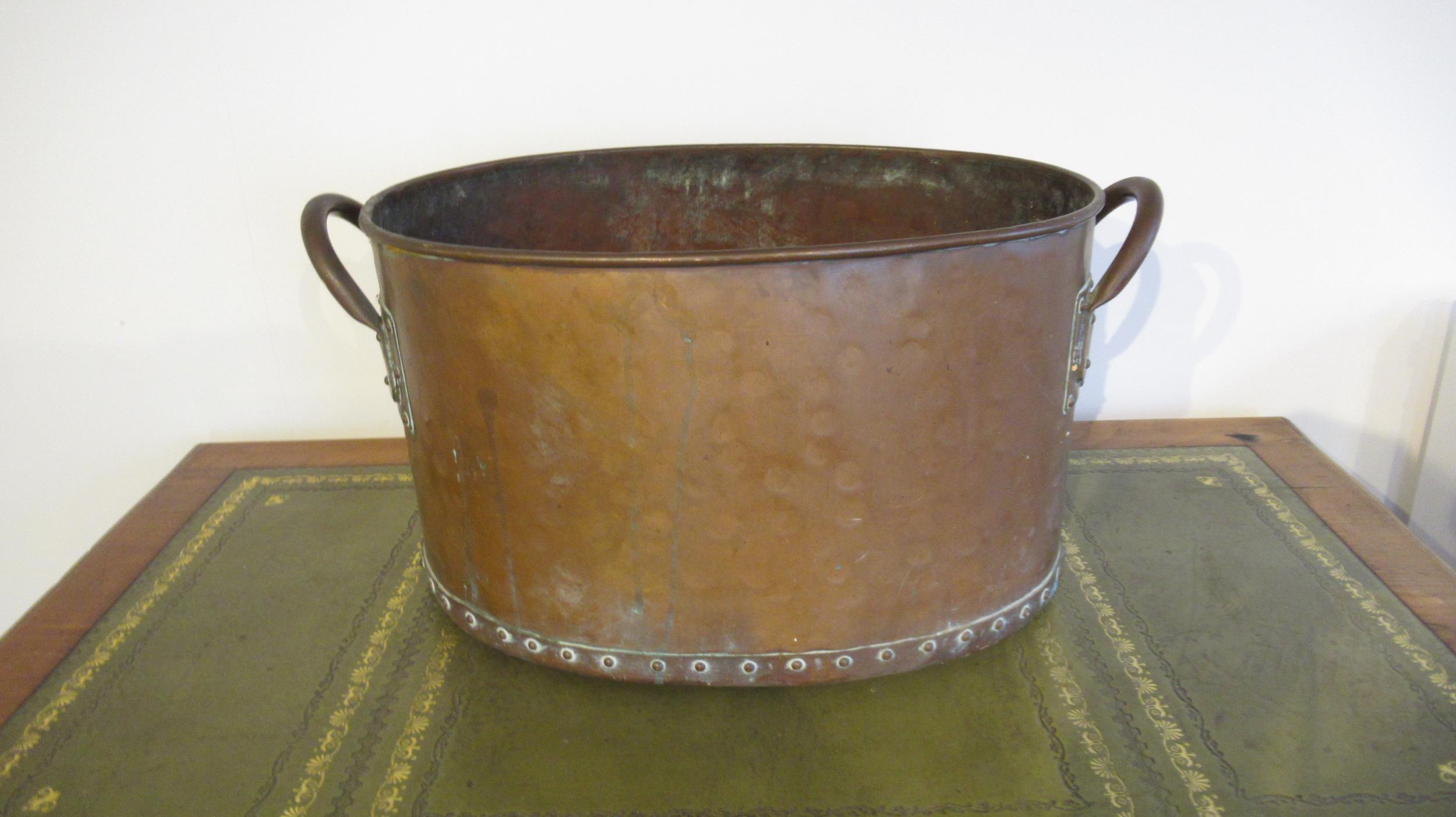 A hand hammered copper log bucket, riveted with twin handles, of oval shape with good patina -