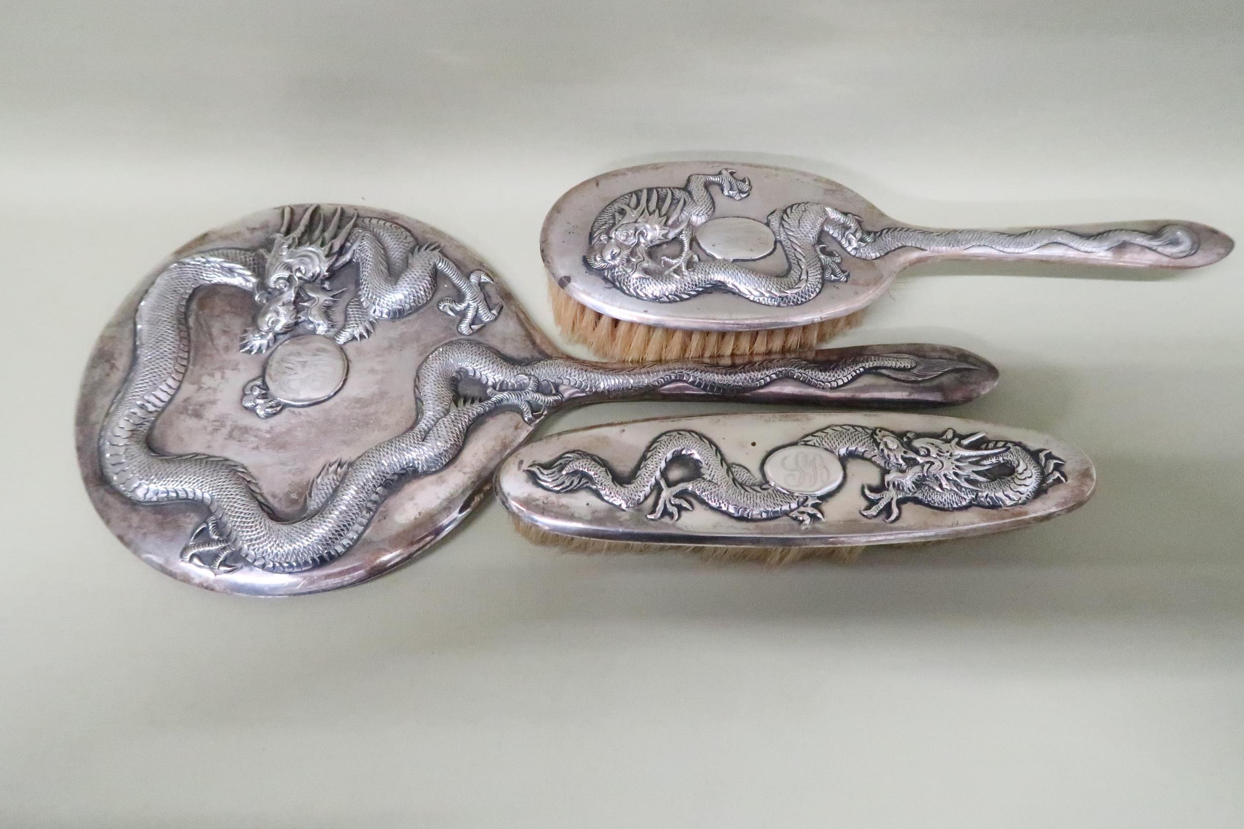 A hand mirror, hairbrush, clothes brush - all in Chinese silver decorated with dragons