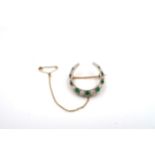 A 9ct gold graduated emerald and diamond crescent brooch. Composed of nine circular emeralds