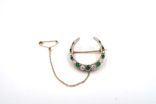 A 9ct gold graduated emerald and diamond crescent brooch. Composed of nine circular emeralds