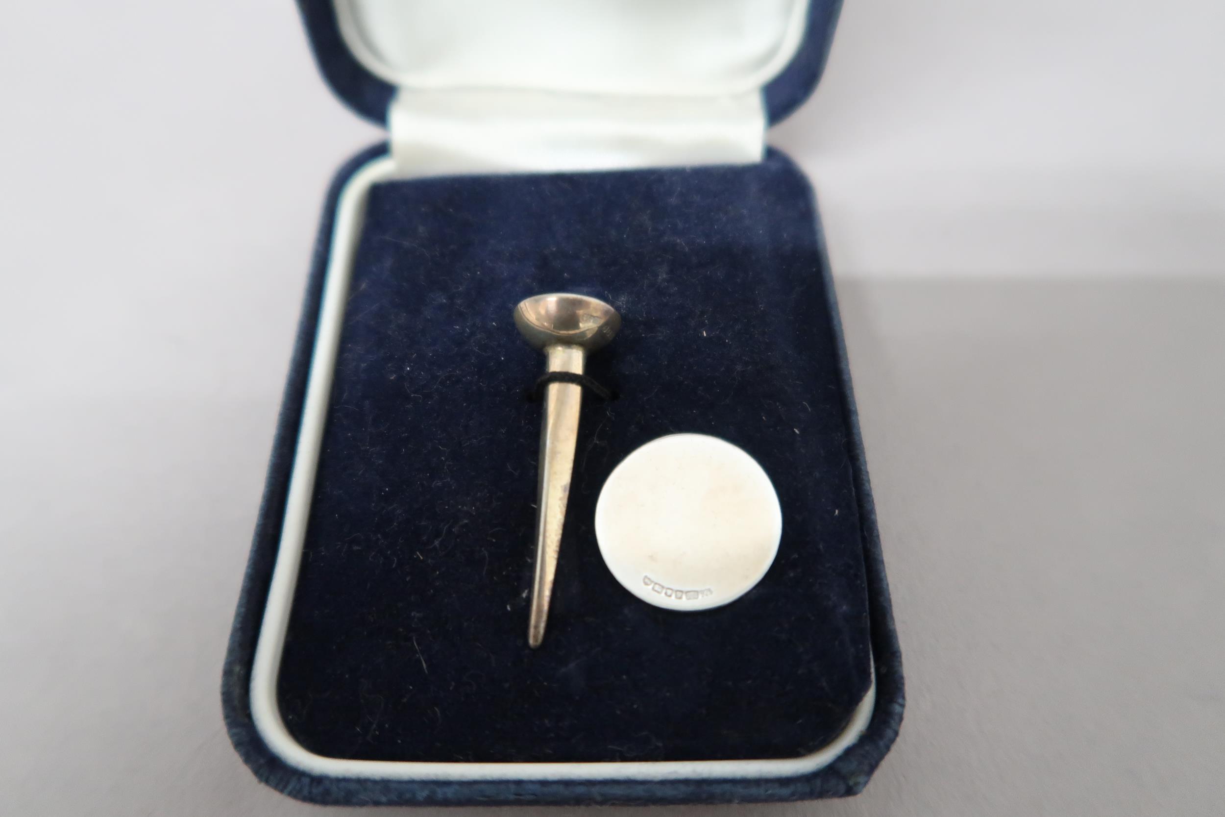 A silver golf tee and ball marker, cased