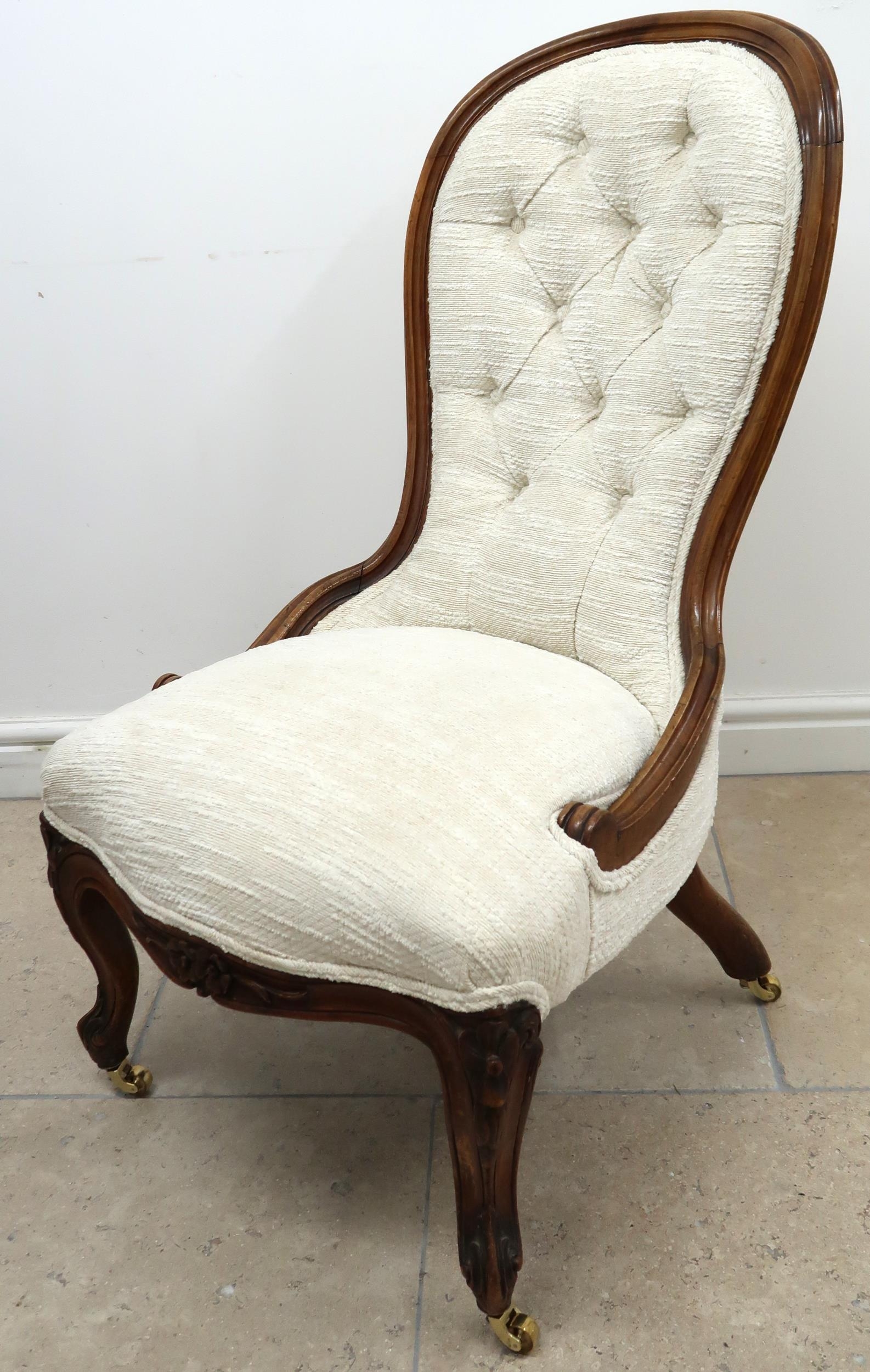 A walnut framed spoon back nursing chair, button upholstery in white raised on casters.