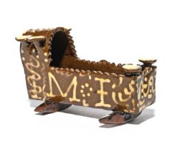 A slipware model of a cradle, dated 1847, decorated in cream slip on a dark brown ground with the