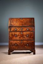A SMALL GEORGE II BURR WALNUT BUREAU C.1735 with cross and feather banding, the hinged fall with