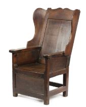 A GEORGE III OAK LAMBING CHAIR LATE 18TH CENTURY with a panelled back flanked by wings and scroll