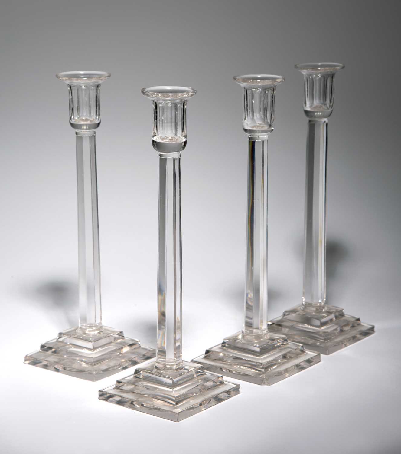 A SET OF FOUR GLASS CANDLESTICKS 20TH CENTURY the fluted stems rising from stepped square bases,