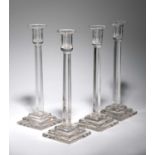 A SET OF FOUR GLASS CANDLESTICKS 20TH CENTURY the fluted stems rising from stepped square bases,