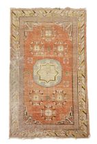 A KHOTAN RUG EAST TURKESTAN, C.1920 the pale terracotta field centred by a rondel framed by six