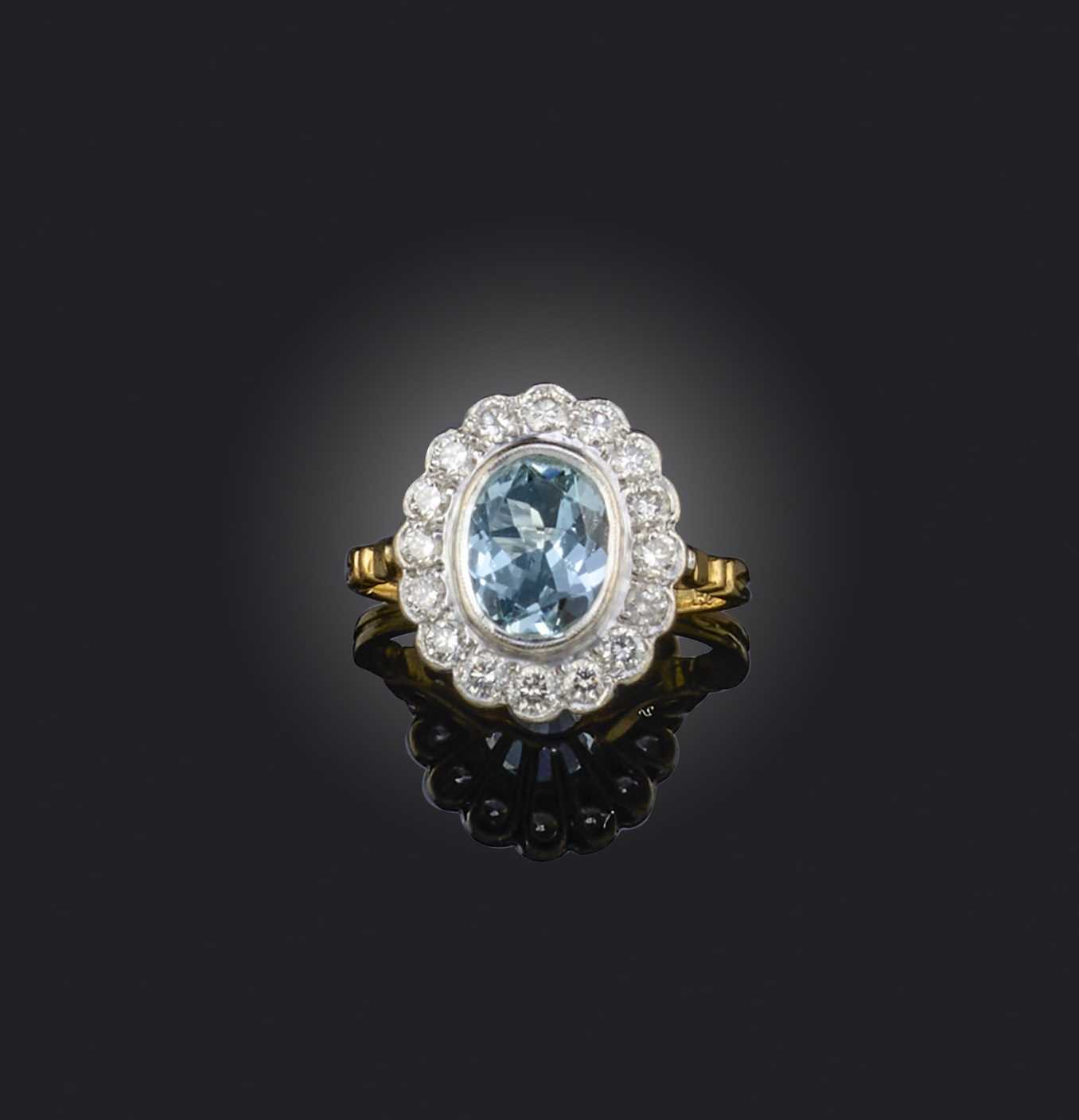 An aquamarine and diamond ring, of cluster design, set with an oval aquamarine, within a border of