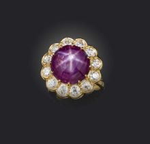 A ruby and diamond cluster ring, the star ruby cabochon set within a surround of circular-cut
