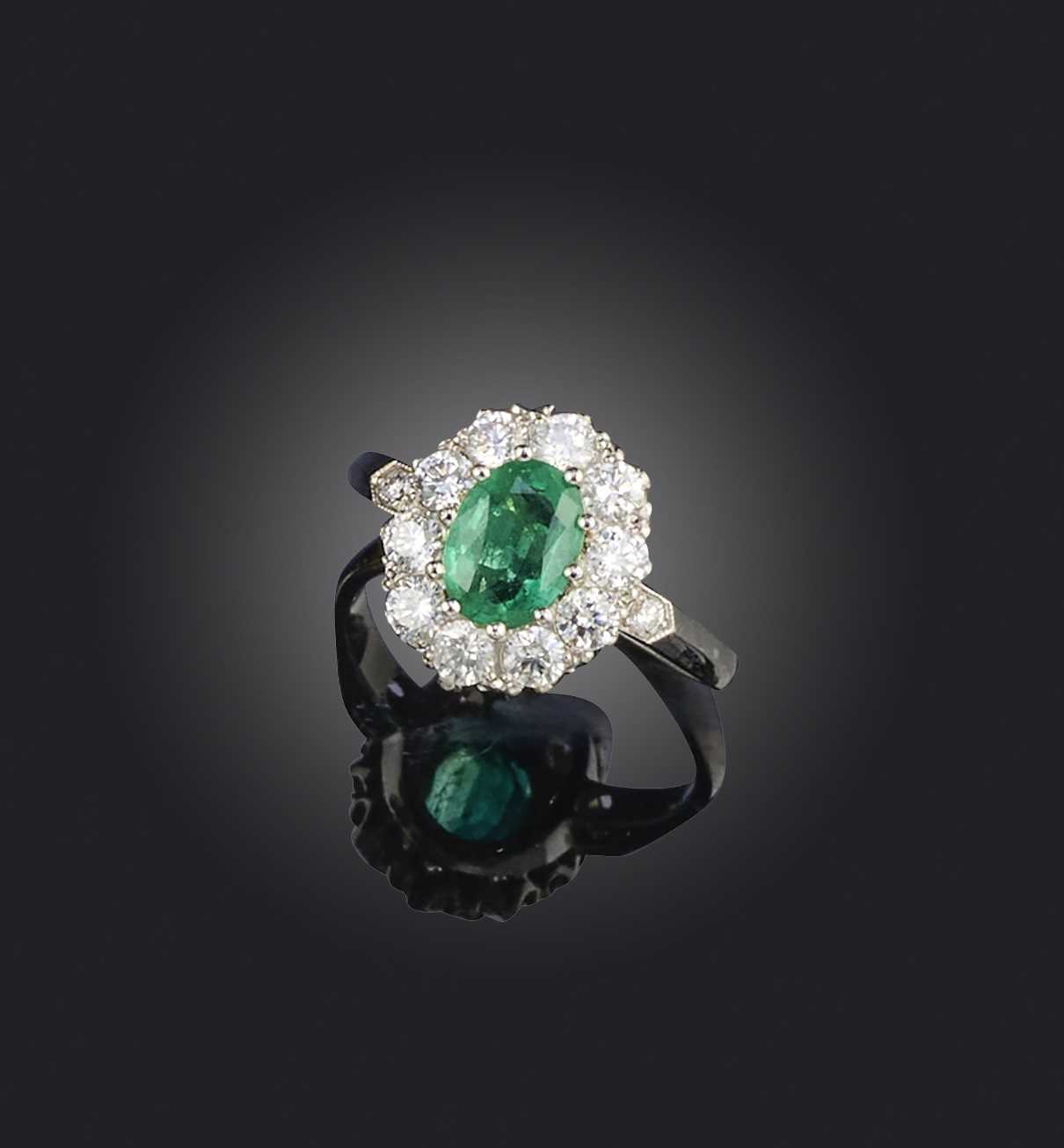 No reserve - an emerald and diamond ring, of cluster design, set with an oval emerald weighing