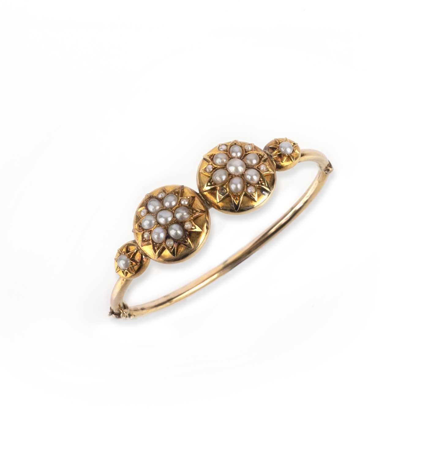 A Victorian gold and half pearl bangle, late 19th century, of hinged design, the front centring on