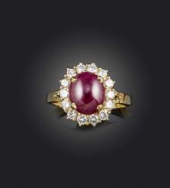 A ruby and diamond ring, of cluster design, set with a cabochon ruby within a border of brilliant-