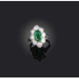 Cartier, an emerald and diamond cluster ring, the oval emerald set within a surround of brilliant-