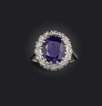 An amethyst and diamond ring, of cluster design, set with an oval amethyst within a border of