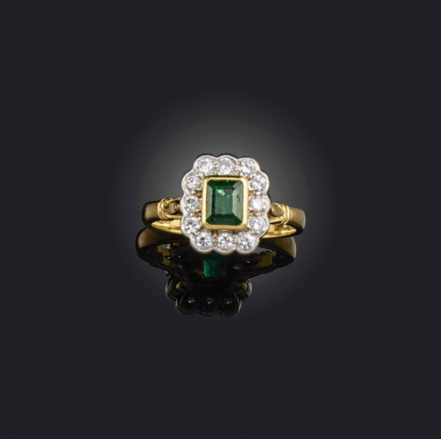 An emerald and diamond ring, of cluster design, set with a step-cut emerald within a border of