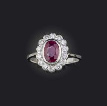 A ruby and diamond cluster ring, the oval-shaped ruby set within a surround of round brilliant-cut