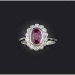 A ruby and diamond cluster ring, the oval-shaped ruby set within a surround of round brilliant-cut