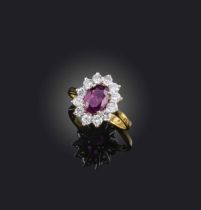 A ruby and diamond cluster ring, the oval-shaped ruby set within a surround of circular-cut diamonds