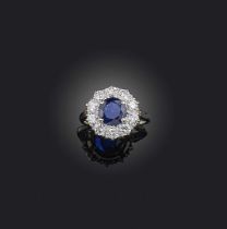 A sapphire and diamond ring, of cluster design, set with a circular-cut sapphire within a border